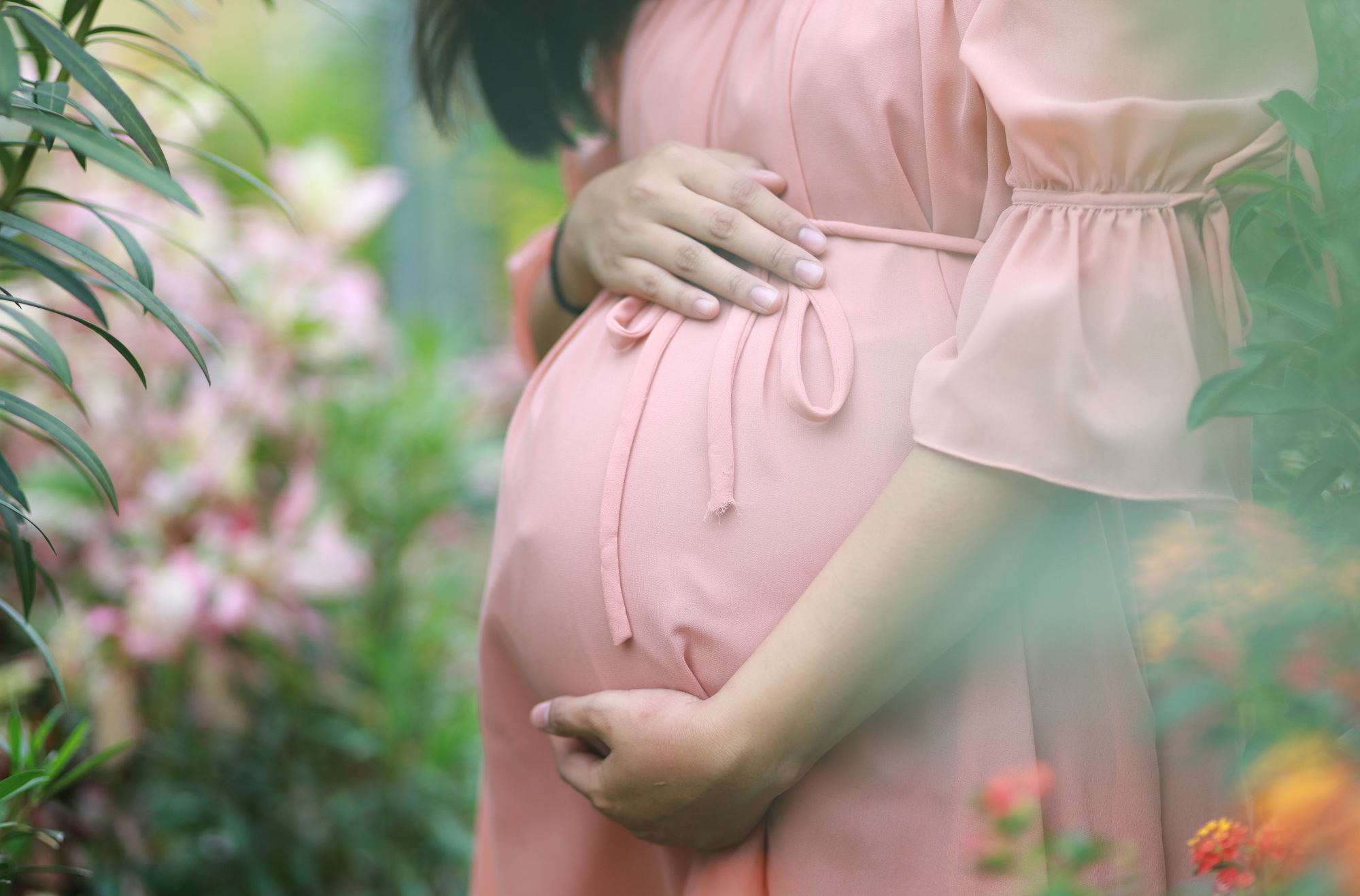 Pregnant woman in pink dress holding her belly
